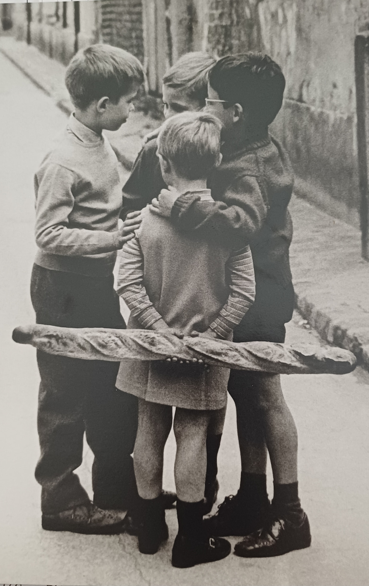 Photographie en noir et blanc : des enfants réunis autour d'une baguette de pain